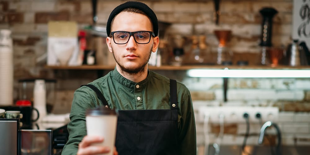 Image: A barista handing you a coffee. Image: A barista handing you a coffee.